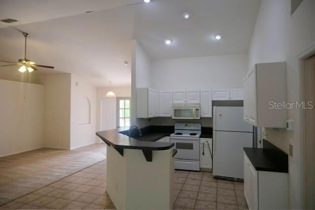 A kitchen with white cabinets and appliances overlooks an adjacent carpeted living area — 1430 SEAPORT STREET, NORTH PORT, FL