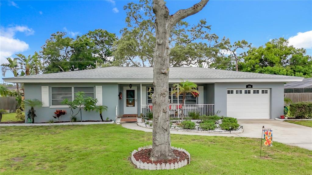 A single-story gray house with a white garage door, a front porch, and a tree — 108 INDIAN ROCKS ROAD S, BELLEAIR BLUFFS, FL