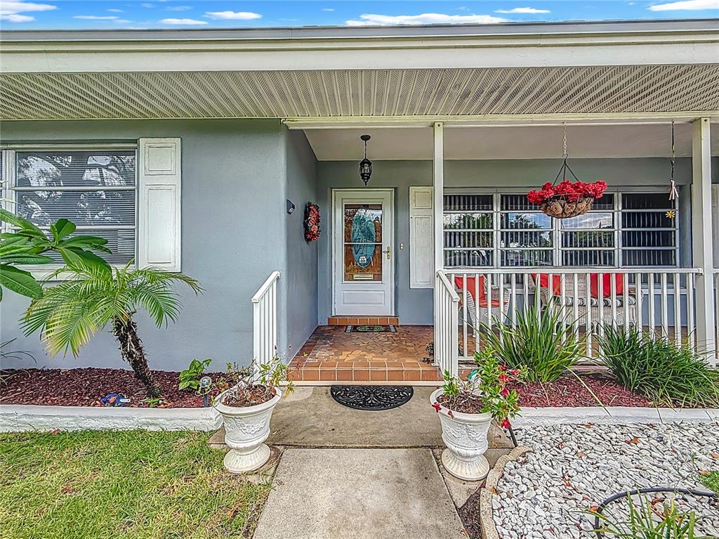 A gray house exterior features a covered porch, a white front door, and two planters — 108 INDIAN ROCKS ROAD S, BELLEAIR BLUFFS, FL