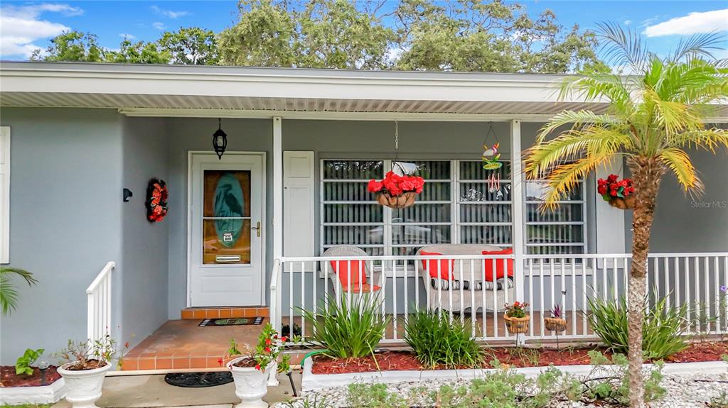 A gray house exterior features a covered front porch with white railings and a palm tree — 108 INDIAN ROCKS ROAD S, BELLEAIR BLUFFS, FL