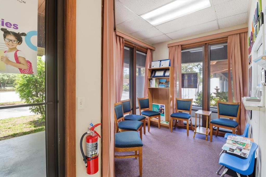 A small waiting room features blue chairs, a bookshelf, and large windows with curtains — 3380 E GULF TO LAKE HIGHWAY UNIT 17, INVERNESS, FL