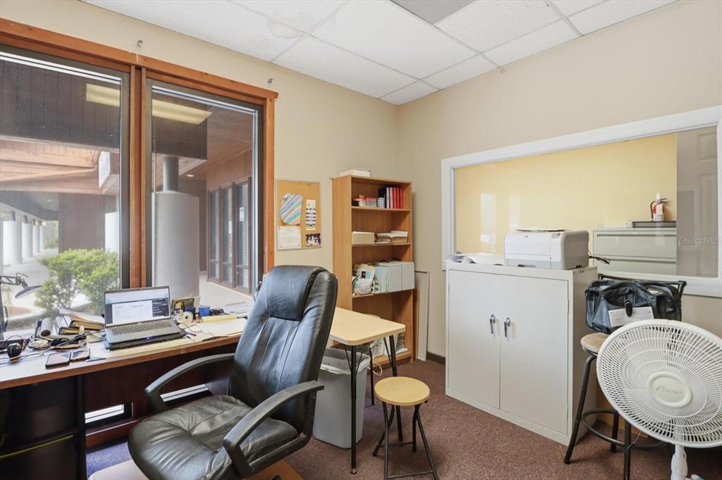 An office space features a desk, black leather chair, bookshelf, and a windowed partition wall — 3380 E GULF TO LAKE HIGHWAY UNIT 17, INVERNESS, FL