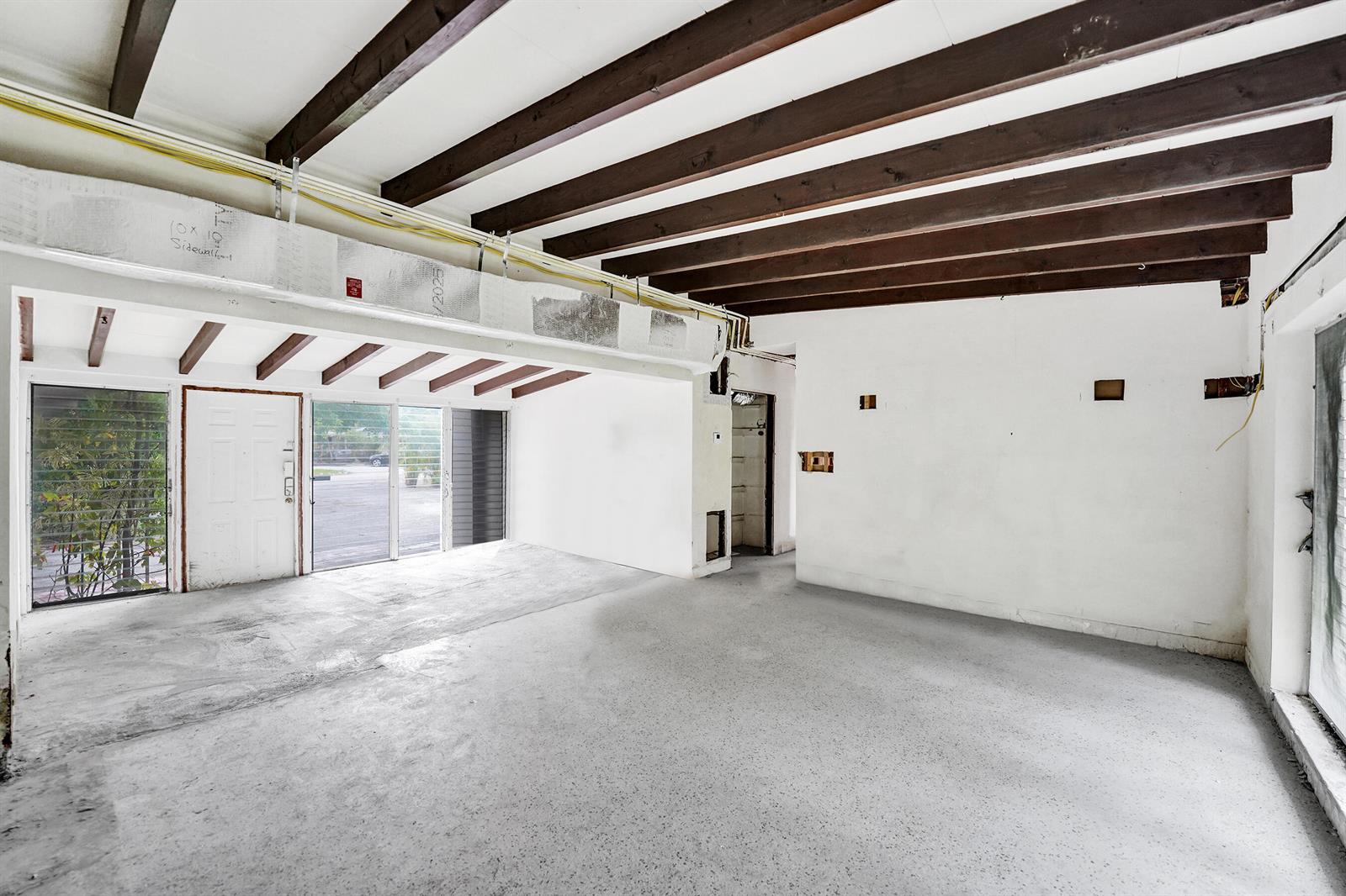 An unfinished room with exposed wooden ceiling beams, concrete flooring, and a white entry door — 2024 NE 26th Drive, Wilton Manors FL 33306, WILTON MANORS, FL