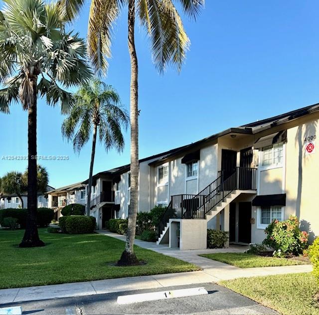 A two-story apartment building features beige stucco walls, black railings, and palm trees — 4000 Crystal Lake Dr # 112, Deerfield Beach FL 33064, DEERFIELD BEACH, FL