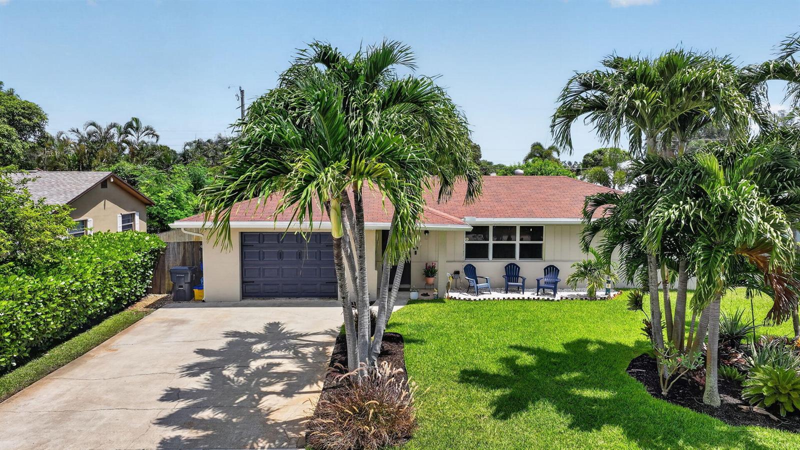 A single-story house with a garage, palm trees, and three blue chairs on the lawn — 2843 Worcester Road, Lake Worth FL 33462, LAKE WORTH, FL