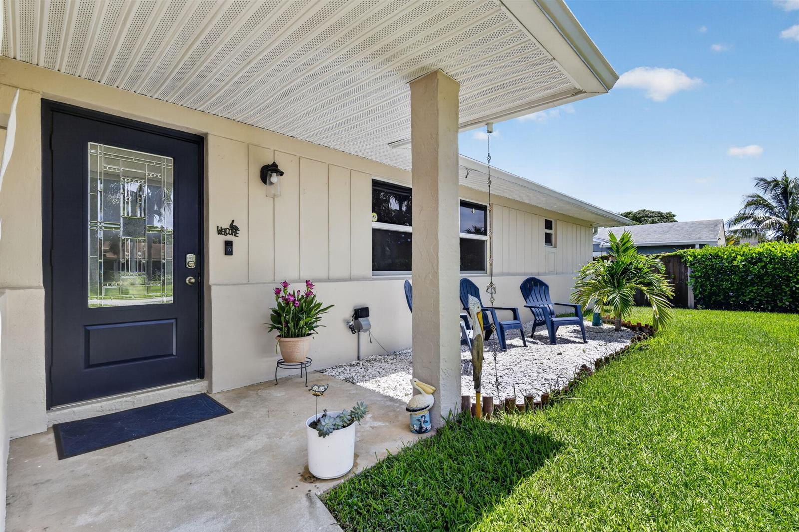 The exterior of a house features a dark front door, a porch, and blue chairs — 2843 Worcester Road, Lake Worth FL 33462, LAKE WORTH, FL