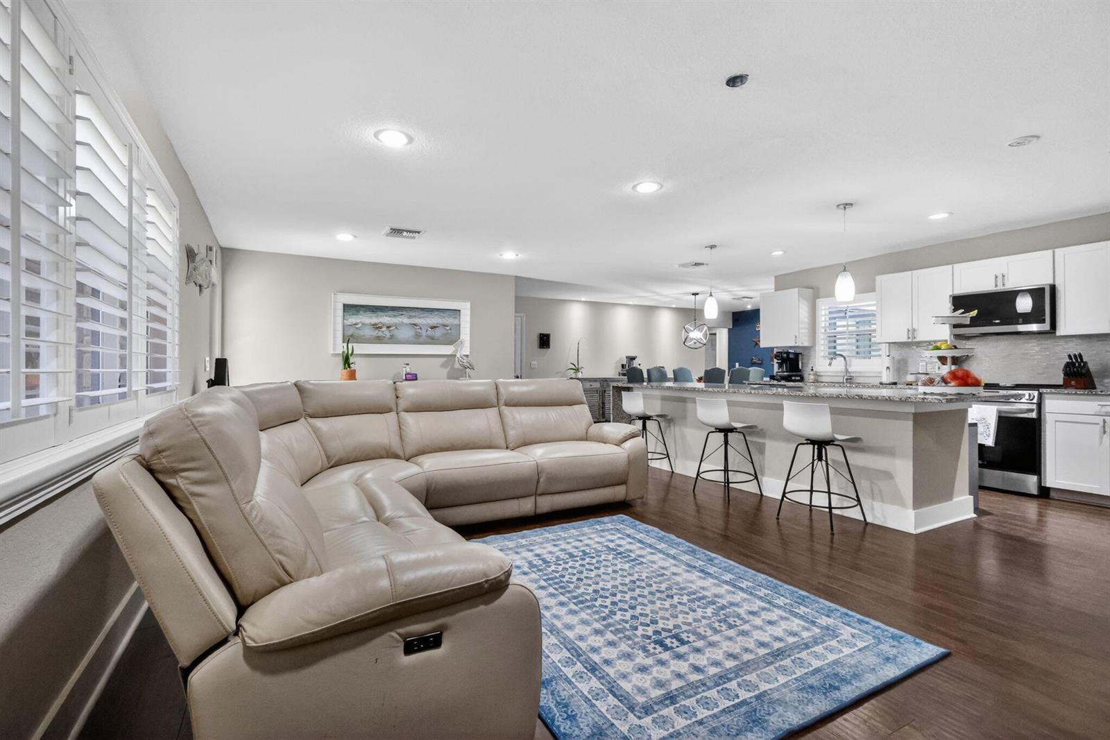 A living room with a beige sectional sofa and blue rug opens to a kitchen — 2843 Worcester Road, Lake Worth FL 33462, LAKE WORTH, FL