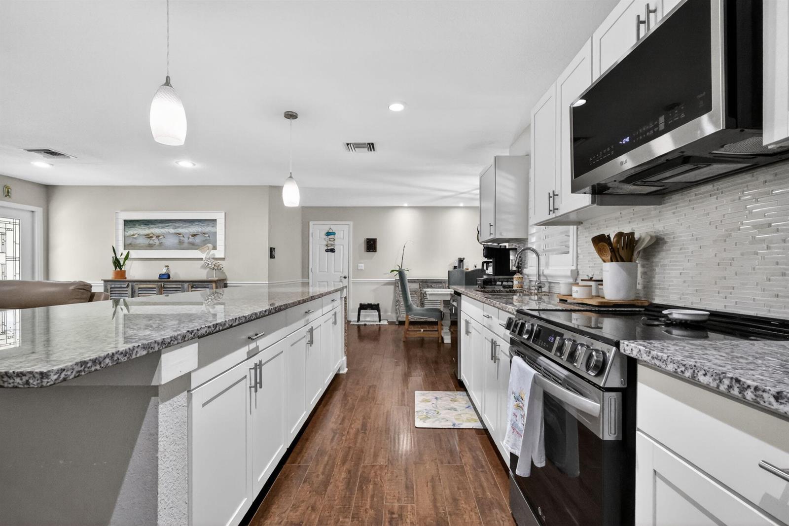 A kitchen features white cabinets, granite countertops, stainless steel appliances, and dark wood flooring — 2843 Worcester Road, Lake Worth FL 33462, LAKE WORTH, FL