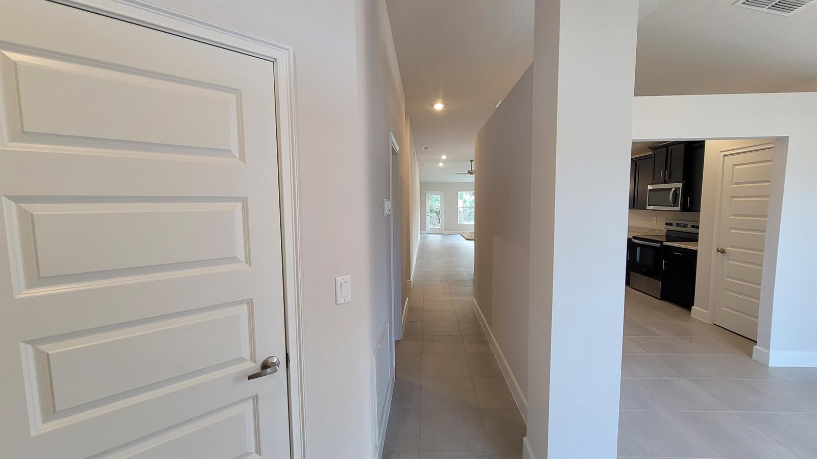 A hallway with light tile flooring leads toward a bright living area and kitchen — 8839 Waterstone Boulevard, Fort Pierce FL 34951, FORT PIERCE, FL