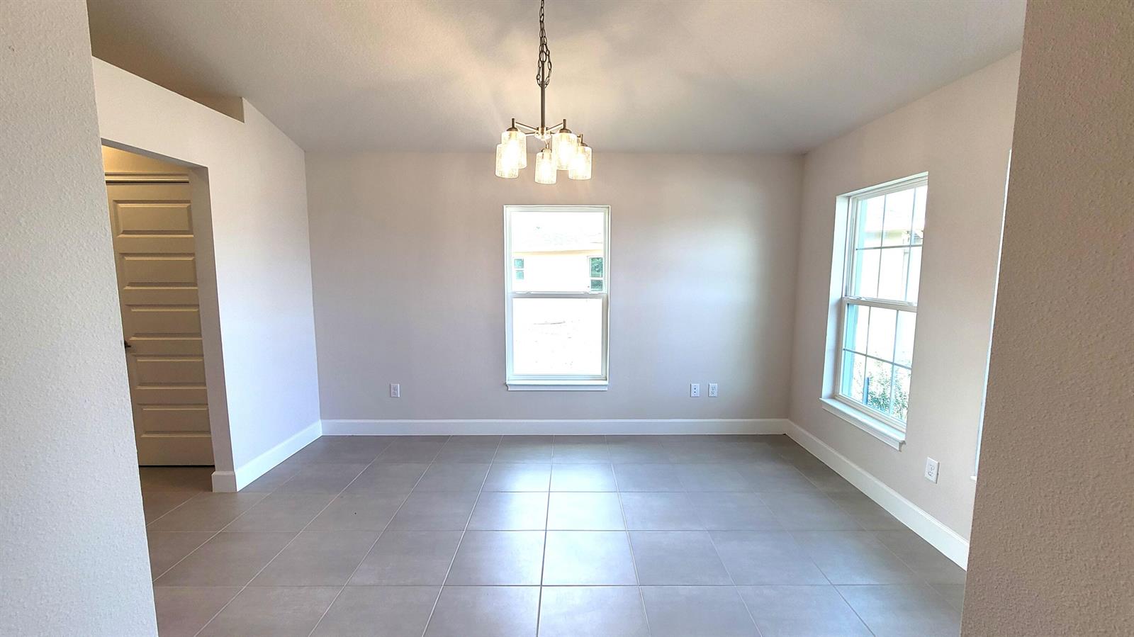 An empty dining room features light-colored walls, large tile flooring, and a central chandelier — 8839 Waterstone Boulevard, Fort Pierce FL 34951, FORT PIERCE, FL