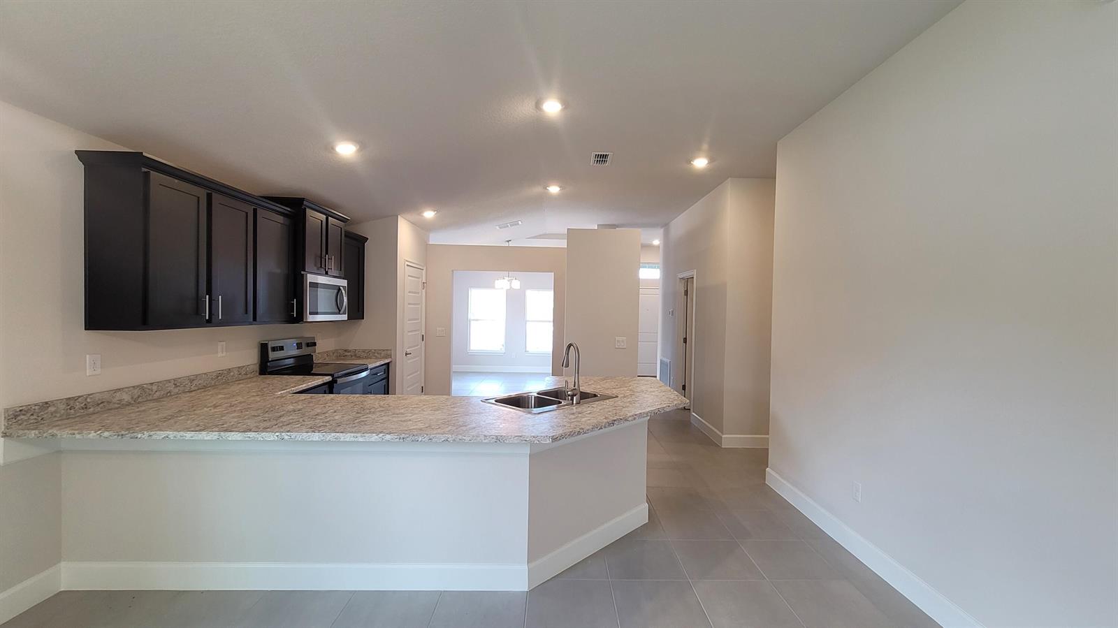 A kitchen features dark cabinets, granite countertops, a breakfast bar, and light tile flooring — 8839 Waterstone Boulevard, Fort Pierce FL 34951, FORT PIERCE, FL