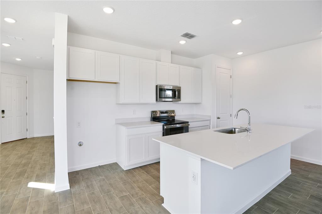A modern kitchen features white cabinets, stainless steel appliances, and a large quartz-topped island — 6195 SW 64TH TERRACE, OCALA, FL