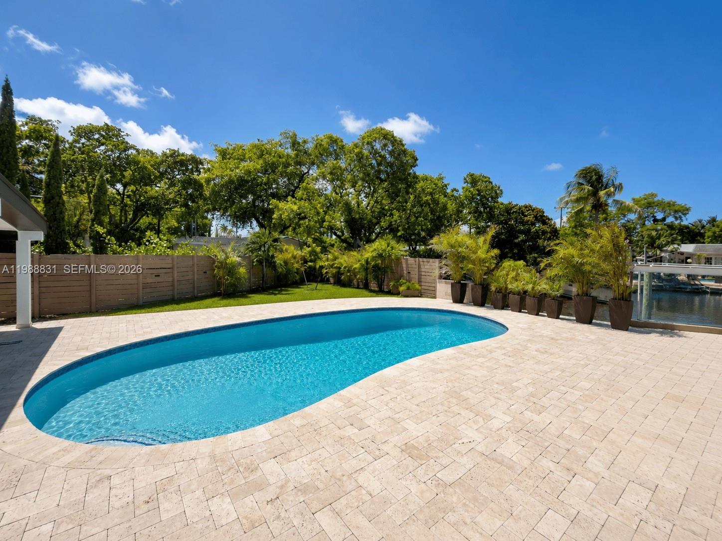 A kidney-shaped swimming pool sits on a stone patio next to a fenced lawn — 1805 Keystone Blvd, North Miami FL 33181, NORTH MIAMI, FL
