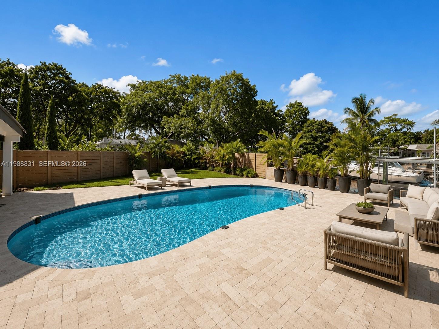 A backyard features a swimming pool, patio furniture, and a wooden fence near a canal — 1805 Keystone Blvd, North Miami FL 33181, NORTH MIAMI, FL