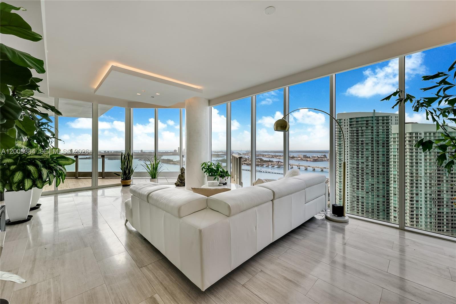 A modern living room features a white sectional sofa, floor-to-ceiling windows, and panoramic water views — 2020 N Bayshore Dr # 3902, Miami FL 33137, MIAMI, FL