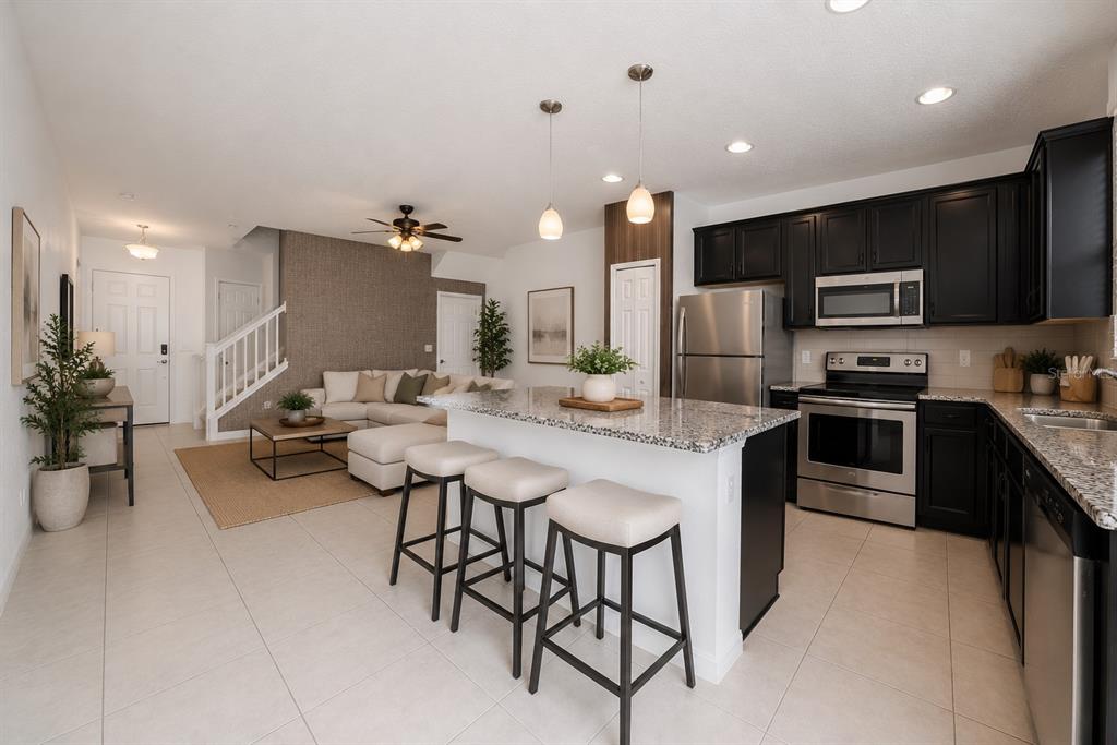 An open-concept kitchen and living area features a granite island, dark cabinets, and tile flooring — 2588 SEDGE GRASS WAY, ORLANDO, FL