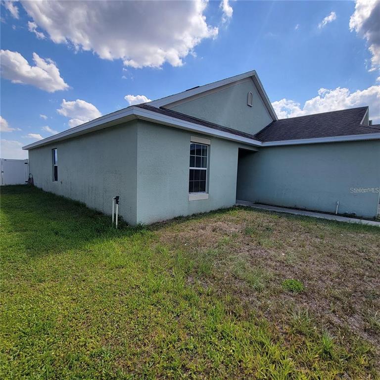 The exterior of a light green stucco house features a gabled roof and a recessed entryway — 30990 SATINLEAF RUN, BROOKSVILLE, FL