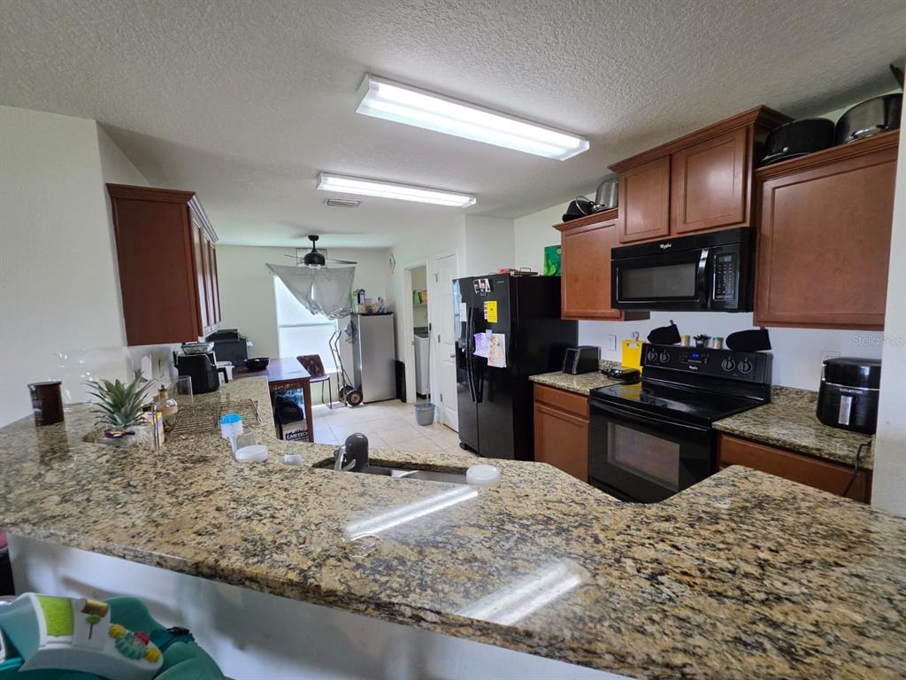 A kitchen features granite countertops, dark wood cabinets, black appliances, and a breakfast bar — 30990 SATINLEAF RUN, BROOKSVILLE, FL