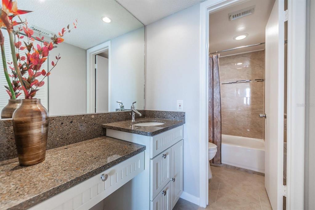 A bathroom featuring a granite vanity countertop, white cabinetry, a large mirror, and a shower-tub — 6219 PALMA BOULEVARD S UNIT 305, ST PETERSBURG, FL