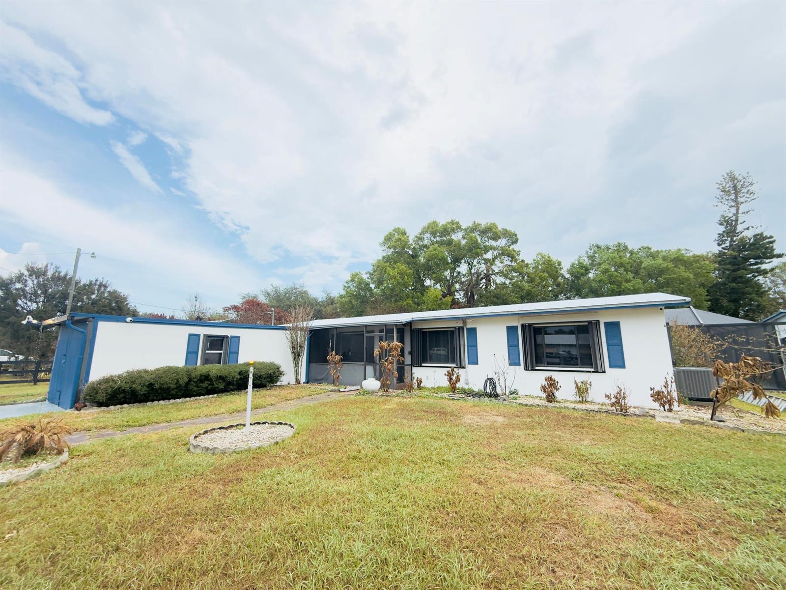 A single-story white house with blue shutters and a screened-in porch sits on a lawn — 4221 Rose Lane NE, Fort Pierce FL 34982, FORT PIERCE, FL