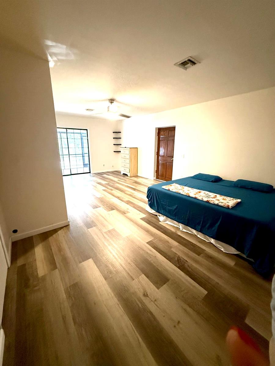 A bedroom with wood-look flooring, a blue bed, and a door leading to a patio — 4221 Rose Lane NE, Fort Pierce FL 34982, FORT PIERCE, FL