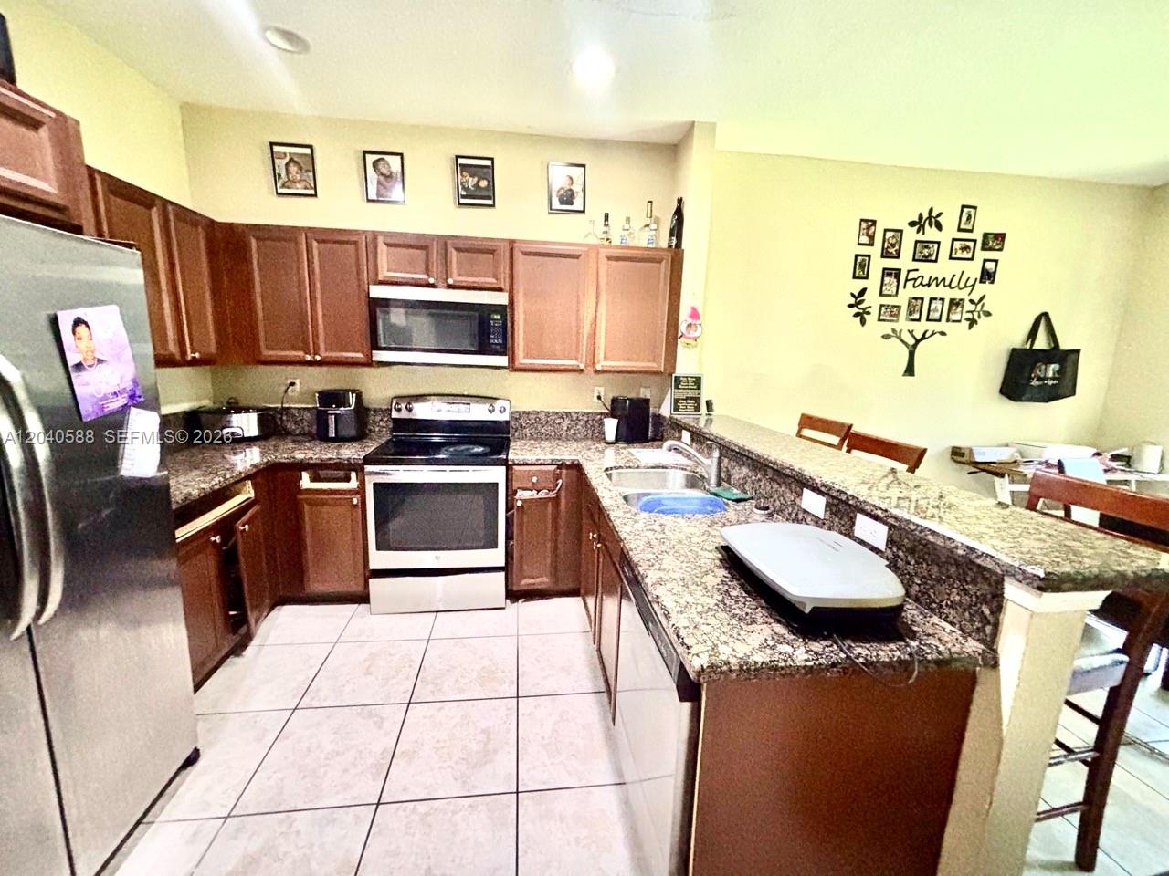 A kitchen features wood cabinets, granite countertops, stainless steel appliances, and tile flooring — MIAMI GARDENS, FL