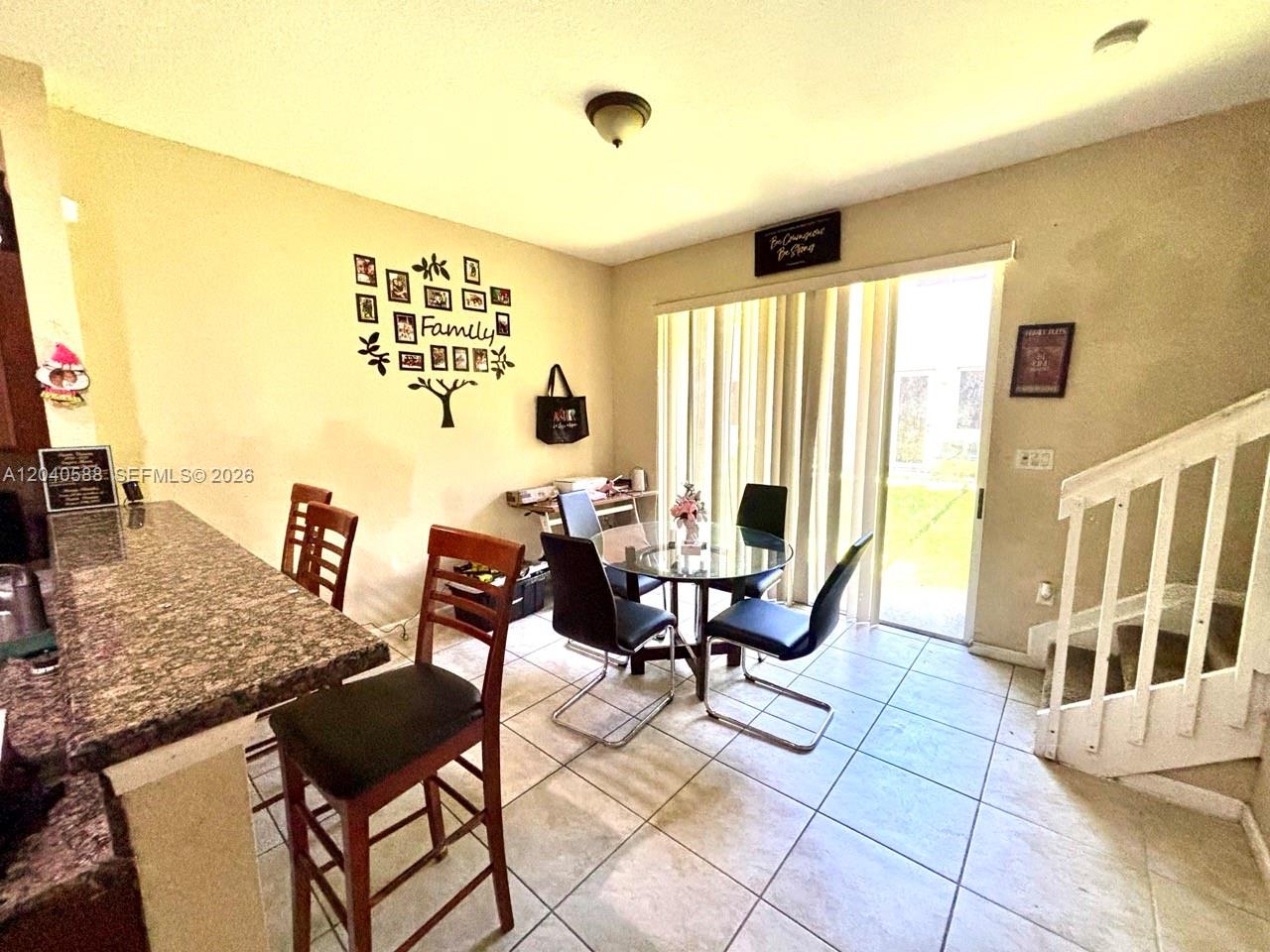 A dining area features a glass table, four black chairs, tile flooring, and a staircase — MIAMI GARDENS, FL