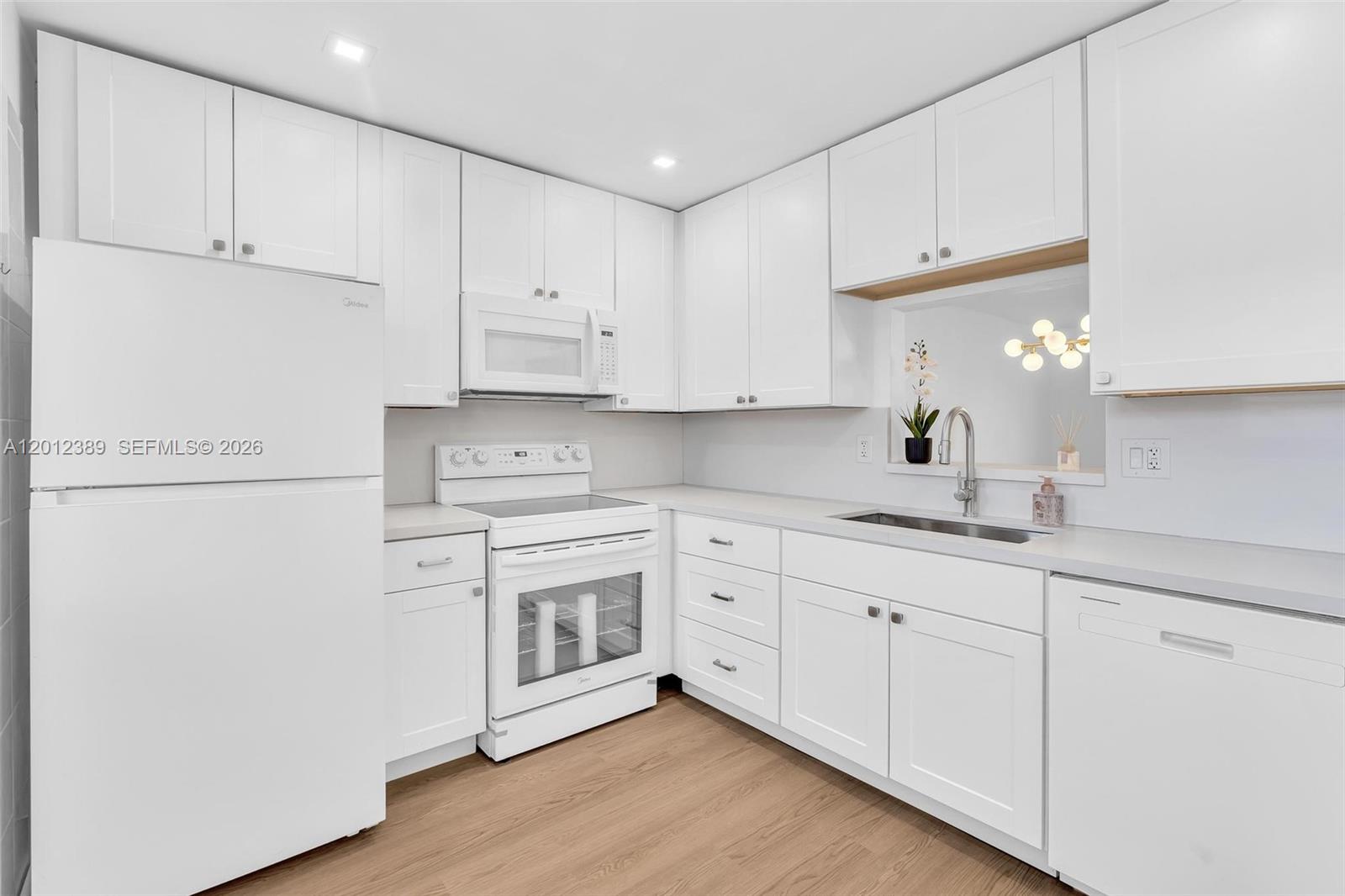 A white kitchen features shaker-style cabinets, stainless steel appliances, and light wood-look flooring — 218 NE 12th Ave # 302, Hallandale Beach FL 33009, HALLANDALE BEACH, FL
