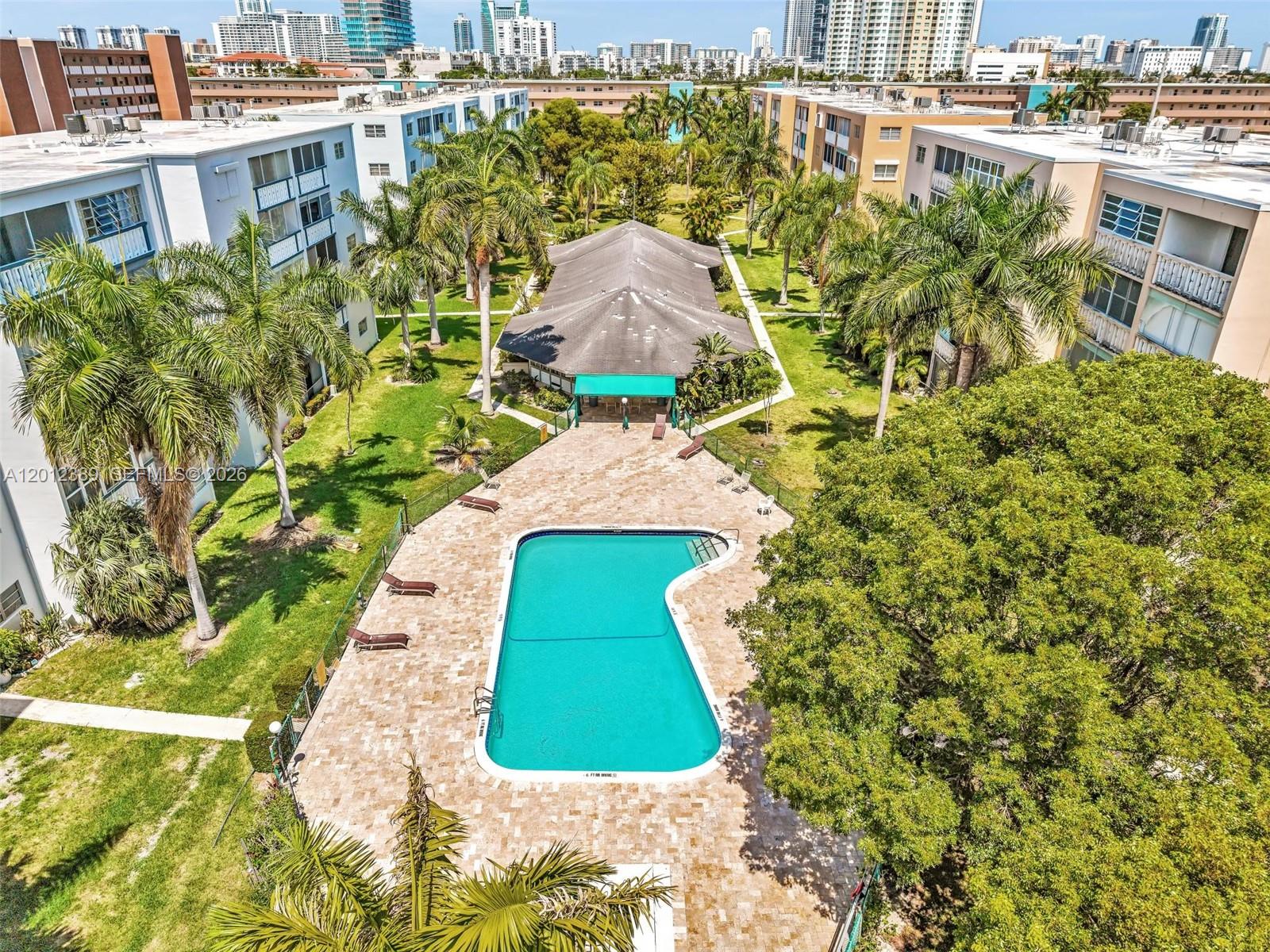 An aerial view shows a swimming pool surrounded by a patio, palm trees, and buildings — 218 NE 12th Ave # 302, Hallandale Beach FL 33009, HALLANDALE BEACH, FL