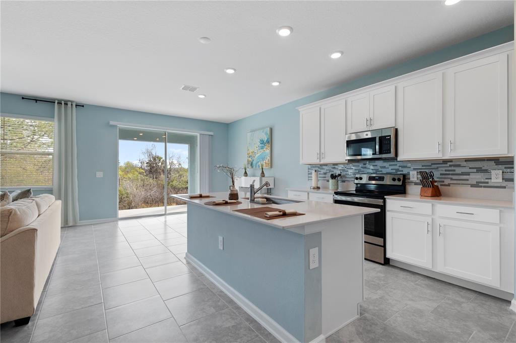 A kitchen with white cabinets, a central island, and light blue walls, opening to outdoors — 157 ACES HIGH LANE, DAVENPORT, FL