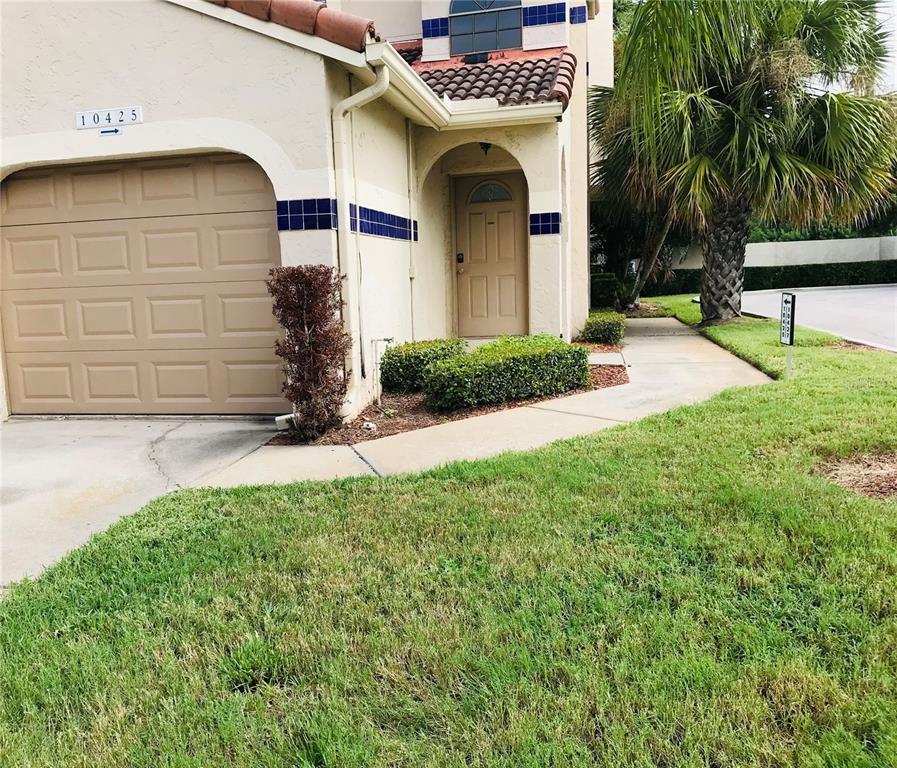 A tan stucco townhouse exterior features a single-car garage, arched entryway, and blue tile accents — 10425 LA MIRAGE COURT UNIT 202, TAMPA, FL