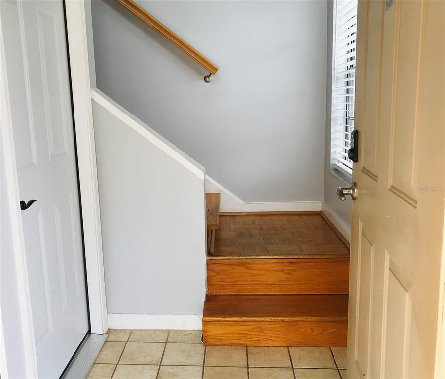 An entryway features a tiled floor, two wooden steps, and a staircase with a handrail — 10425 LA MIRAGE COURT UNIT 202, TAMPA, FL