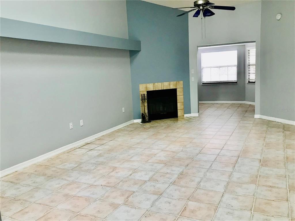 An empty living room features a tiled floor, a fireplace, and a ceiling fan — 10425 LA MIRAGE COURT UNIT 202, TAMPA, FL