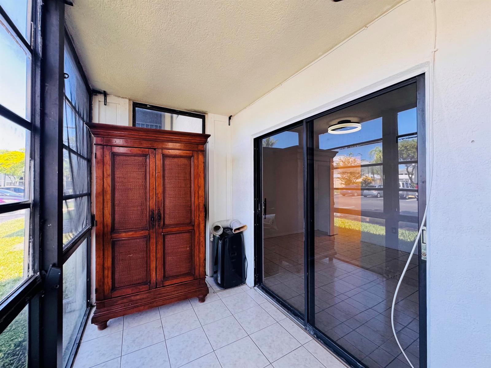 A sunroom features a large wooden armoire, a portable air conditioner, and sliding glass doors — 809 NE 199th Street # 7, Miami FL 33179, MIAMI, FL