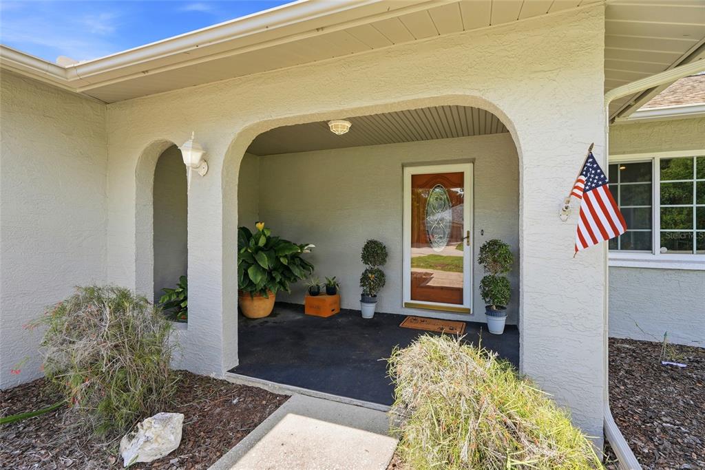 A covered front porch with arched openings, a glass-paneled door, and potted plants — 10435 TASSEL STREET, SPRING HILL, FL