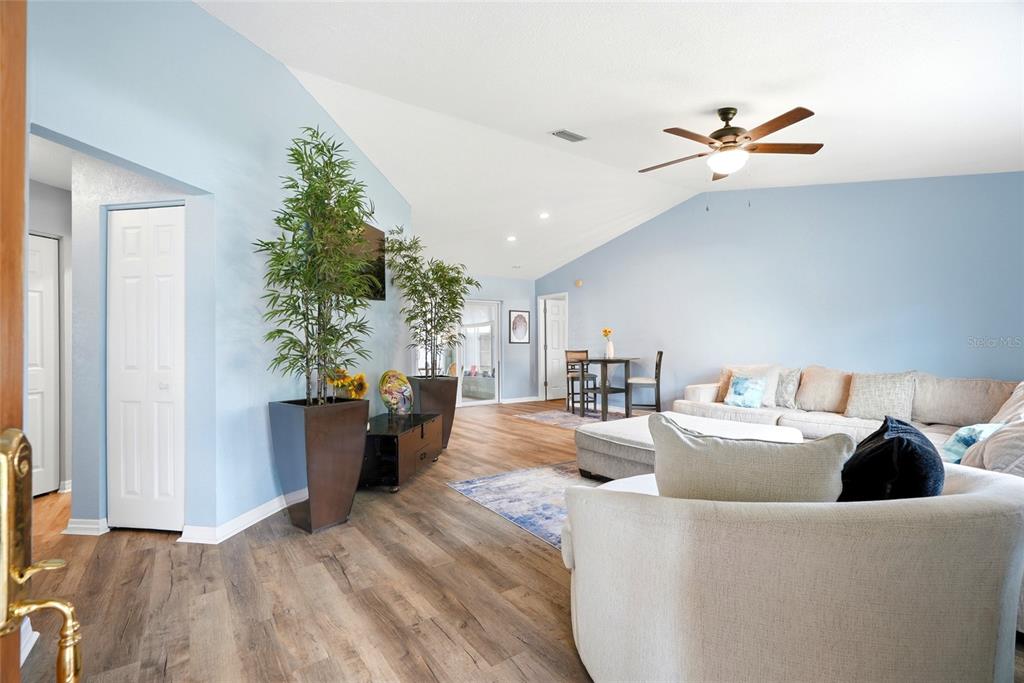 A living room features light blue walls, wood-look flooring, a vaulted ceiling, and furniture — 10435 TASSEL STREET, SPRING HILL, FL