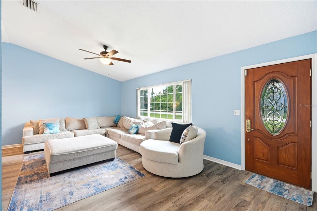 A living room features light blue walls, a sectional sofa, and a wood-paneled front door — 10435 TASSEL STREET, SPRING HILL, FL