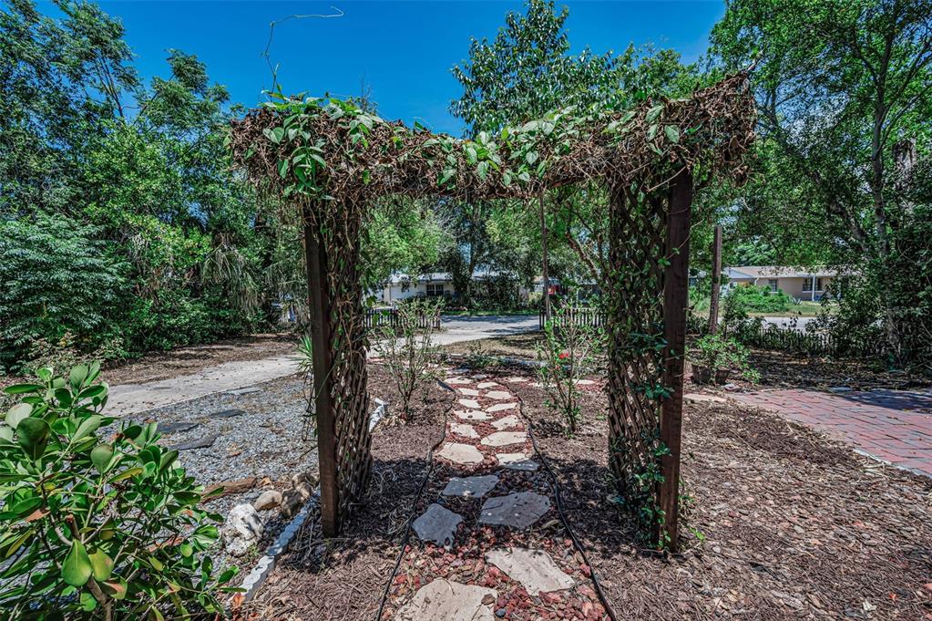 A wooden garden arbor stands over a stone path in a landscaped yard — 4312 BEACON SQUARE DRIVE, HOLIDAY, FL