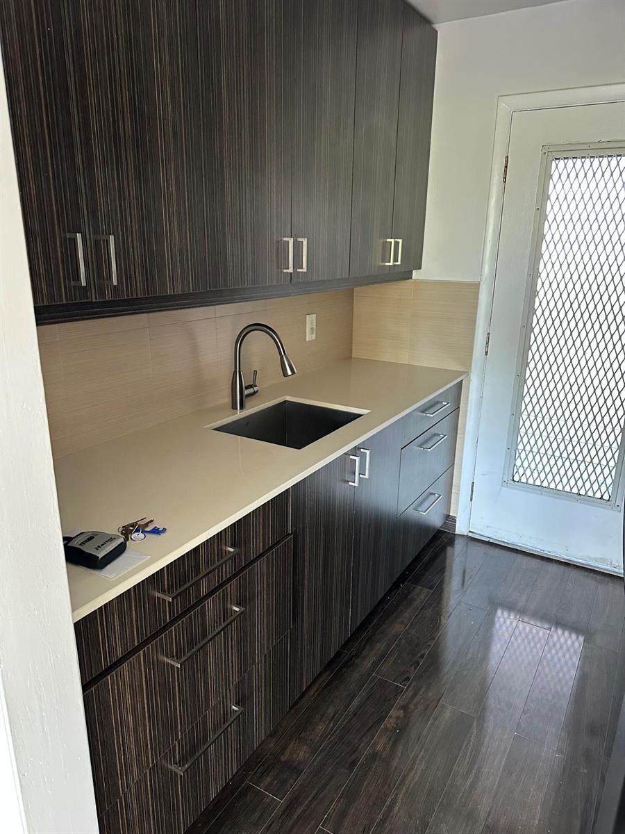 A kitchen kitchenette featuring dark wood-grain cabinets, a light countertop, and a stainless steel sink — 1480 E Sample Road # 207, Pompano Beach FL 33064, POMPANO BEACH, FL
