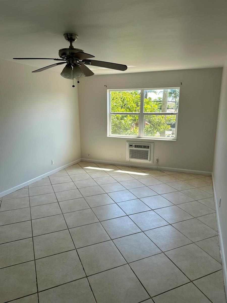 An empty bedroom with beige tile flooring, a ceiling fan, and a window air conditioner — 1480 E Sample Road # 207, Pompano Beach FL 33064, POMPANO BEACH, FL