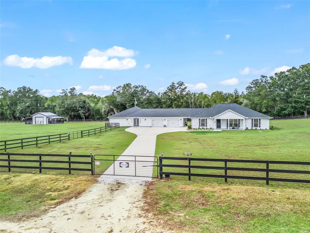 A white ranch-style house with a concrete driveway sits behind a black metal gate — 6570 SE 175TH COURT, MORRISTON, FL