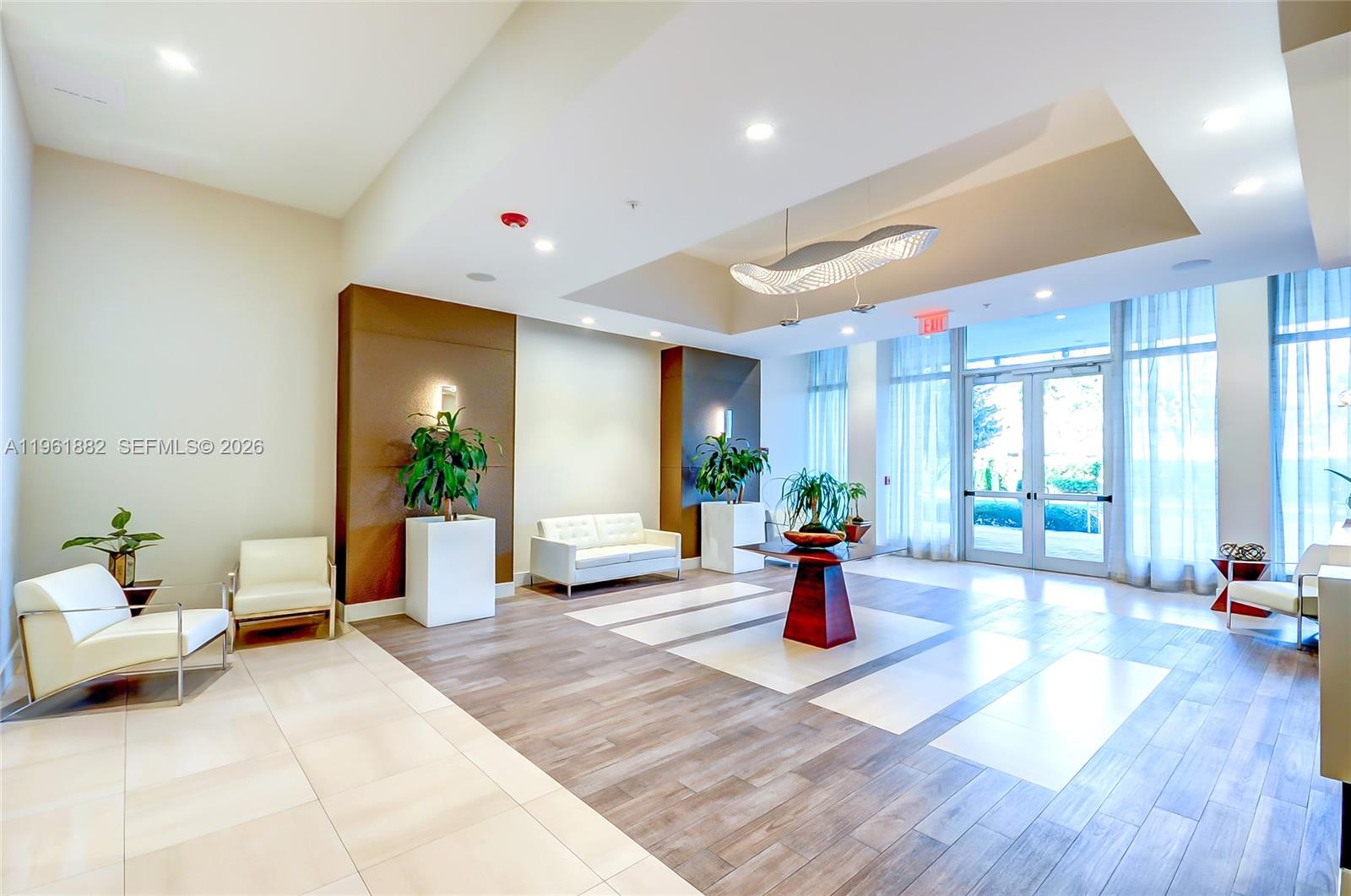 A modern lobby features white tile and wood-look flooring, seating areas, and a central table — 7661 NW 107th Ave # 506, Doral FL 33178, DORAL, FL