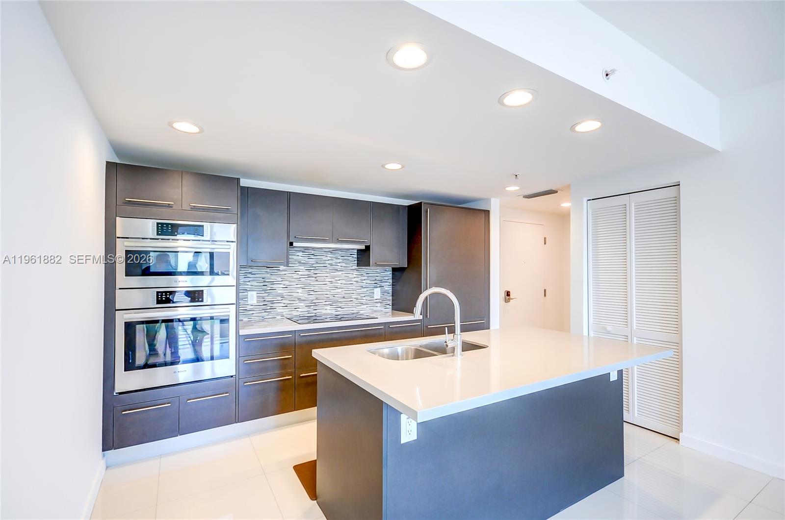 A modern kitchen features dark cabinetry, stainless steel appliances, and a central island with sink — 7661 NW 107th Ave # 506, Doral FL 33178, DORAL, FL