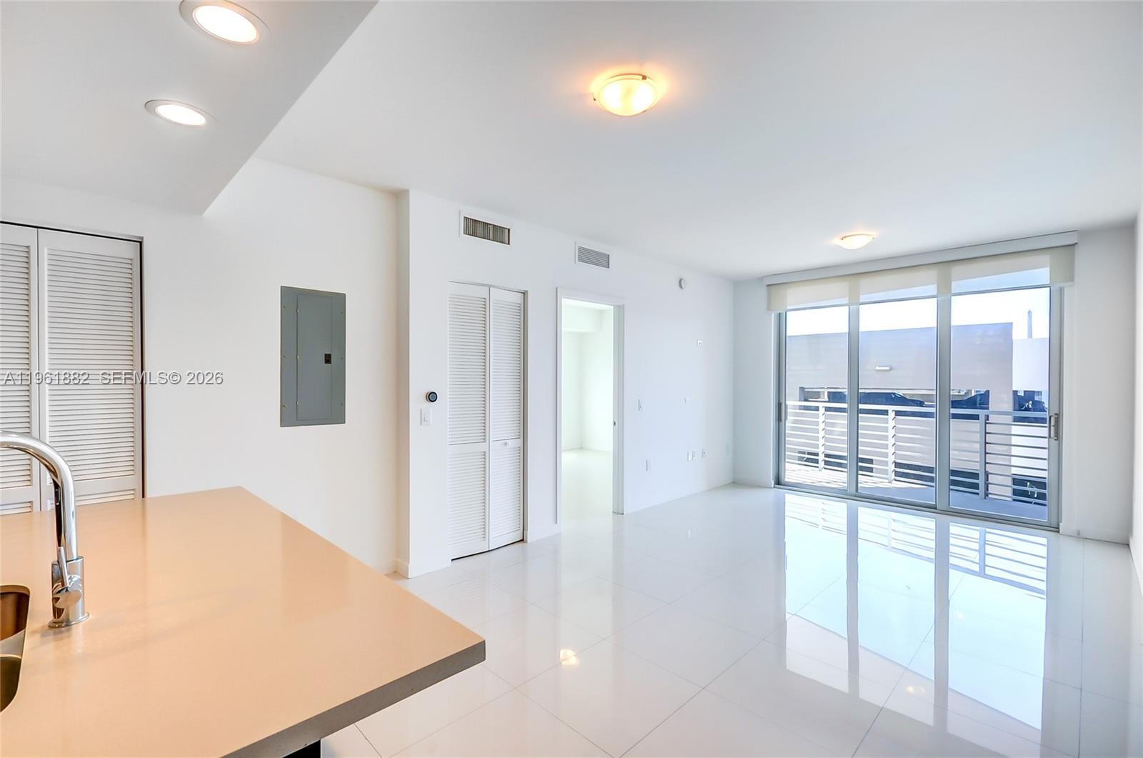 A bright, minimalist living area features white tile floors, recessed lighting, and a sliding glass door — 7661 NW 107th Ave # 506, Doral FL 33178, DORAL, FL