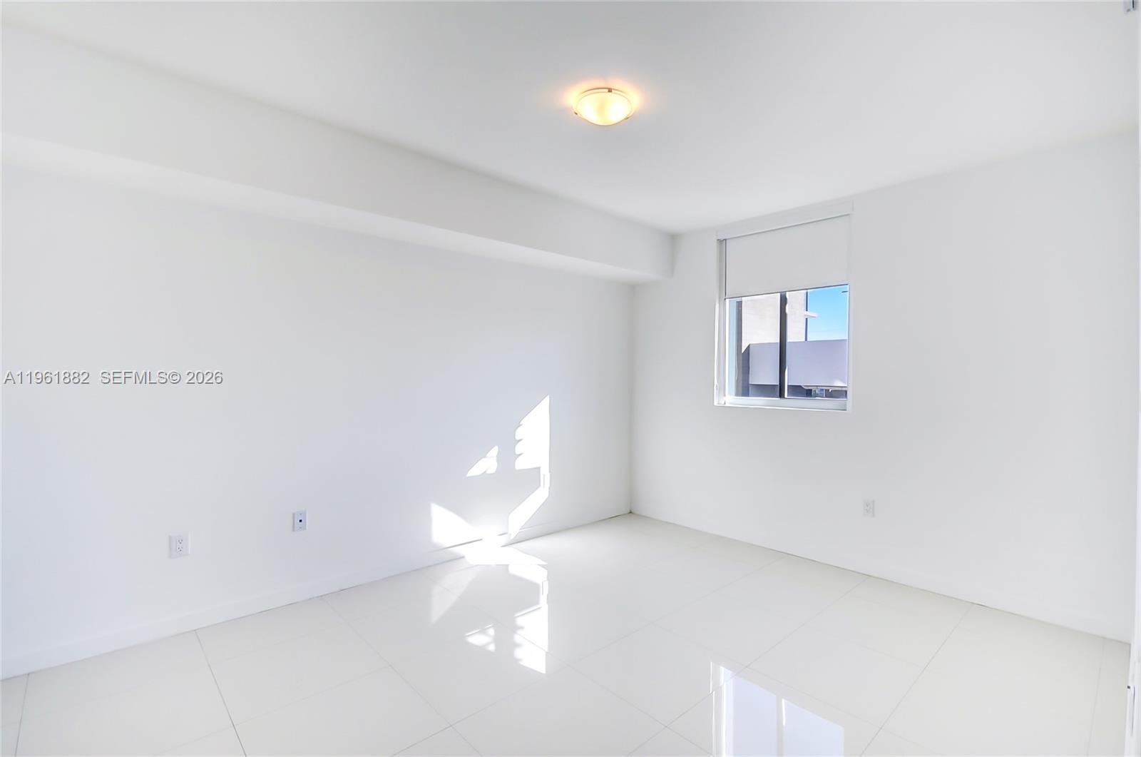 An empty room features white walls, glossy tile flooring, a window, and a ceiling light — 7661 NW 107th Ave # 506, Doral FL 33178, DORAL, FL