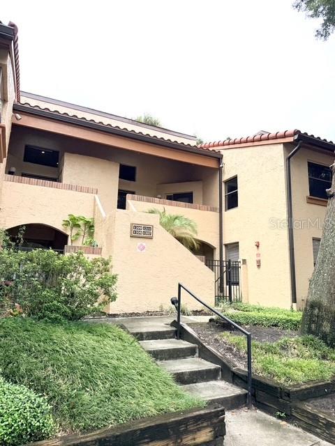A multi-story tan stucco apartment building features a staircase leading to an upper-level walkway — 1211 SALERNO COURT UNIT 1211, ORLANDO, FL