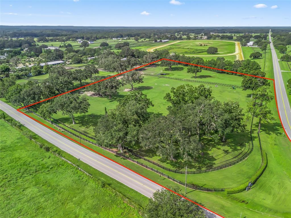 An aerial view shows a fenced, tree-filled pasture bordered by a road and rural landscape — TBD NW 110TH AVE, OCALA, FL