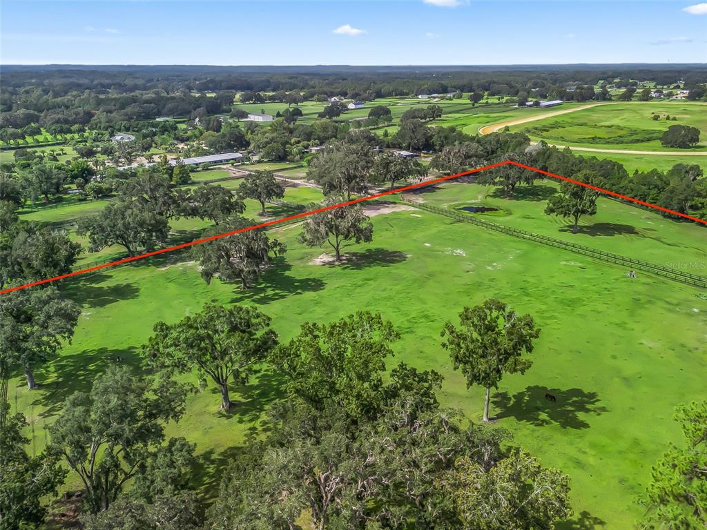 An aerial view shows a large, grassy pasture with scattered trees and fenced boundaries — TBD NW 110TH AVE, OCALA, FL