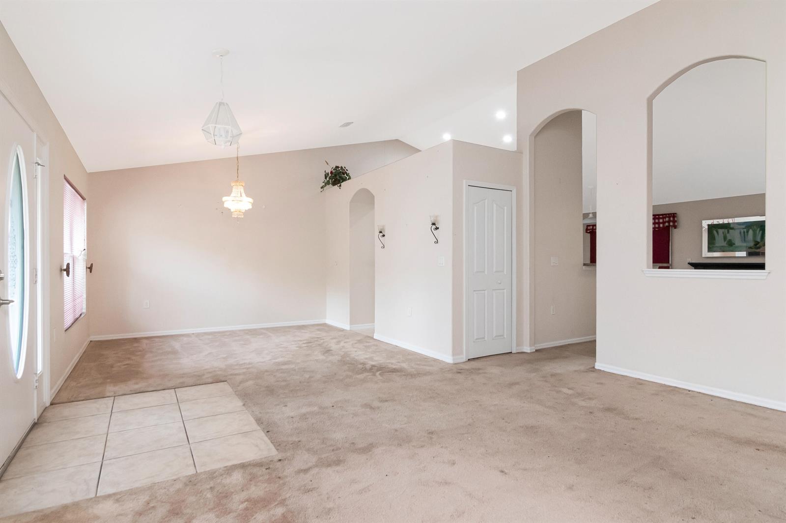 An open-concept living area features beige carpeting, a tiled entryway, and arched wall cutouts — 12276 N Villa Road, Spring Hill FL 34609, SPRING HILL, FL