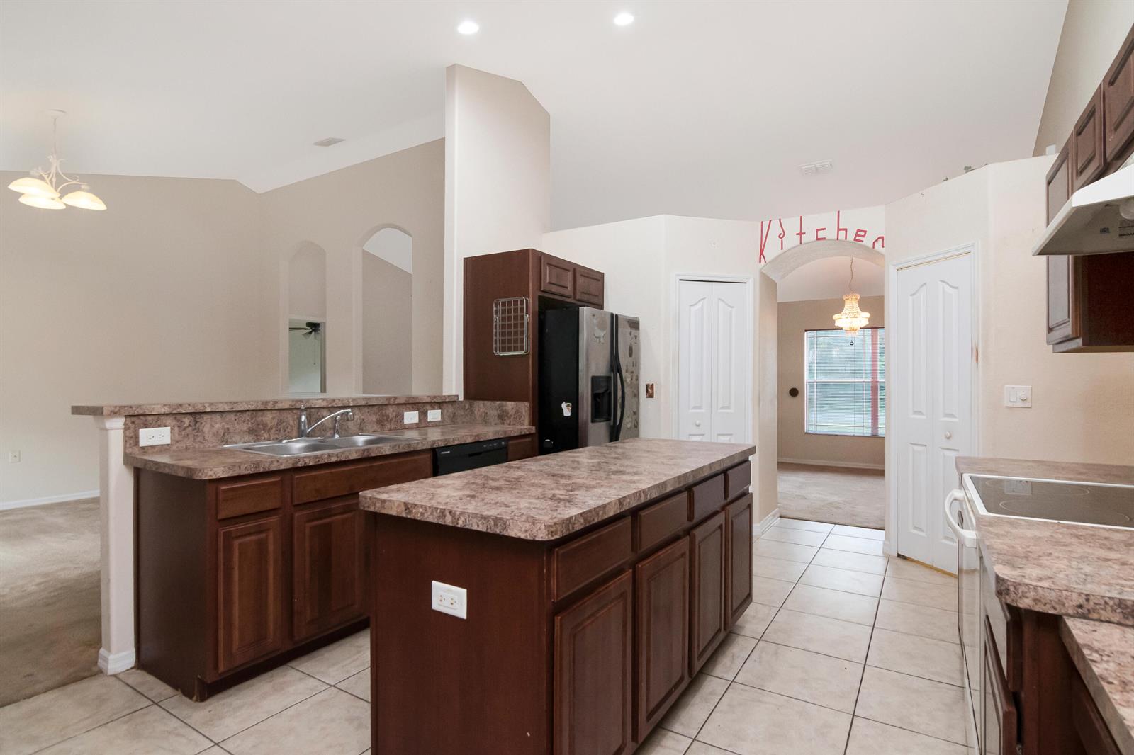A kitchen features dark wood cabinets, laminate countertops, a central island, and tile flooring — 12276 N Villa Road, Spring Hill FL 34609, SPRING HILL, FL